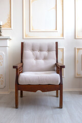 Wooden armchair with a soft white seat stands on the antique beige wall background