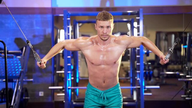 athletic fitness man doing pulling exercises working out in gym with cable tower. Muscular body builder chest fly on the wire cable machine triceps. Shirtless guy doing pectorals on the crossover