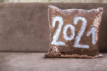 Golden pillow with paillettes on the brown sofa with inscription 2021. Pillow with sequins. Place for text