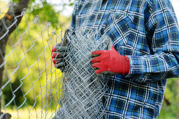 Close up on midsection of unknown man holding protective chain link diamond wire fence in the field...