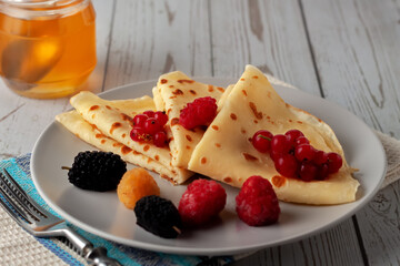 Thin pancakes with honey, raspberries, mulberries and currants