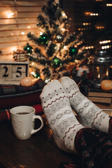 Feet in Christmas socks. Close up on feet. Winter and Christmas holidays concept. The cup of hot drink. Cozy scene. Background with christmas decor. Christmas background.