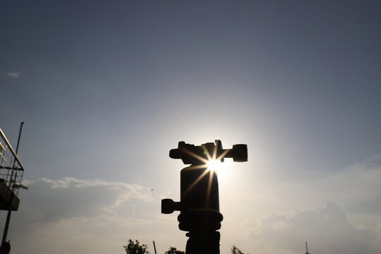Silhouetted Camera tripod close up in front of blue sky and the sun in nature  with some space to write 