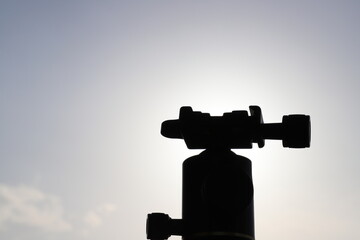 Silhouetted Camera tripod close up in front of blue sky and the sun in nature  with some space to...