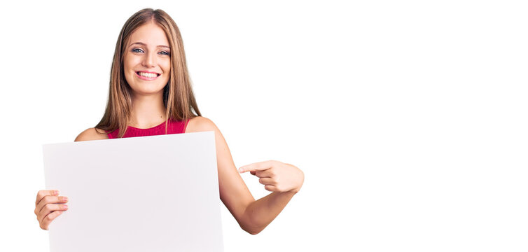 Young beautiful blonde woman holding blank empty banner smiling happy pointing with hand and finger