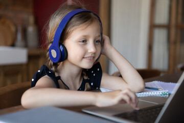 Confident user. Happy little child girl spending time at home using laptop and headphones, studying...