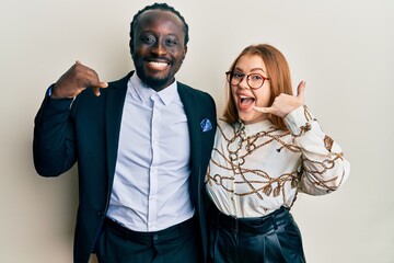Young interracial couple wearing business and elegant clothes smiling doing phone gesture with hand and fingers like talking on the telephone. communicating concepts.