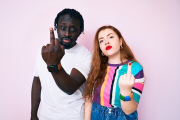 Interracial couple wearing casual clothes showing middle finger, impolite and rude fuck off expression