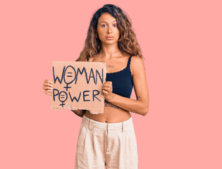 Young hispanic woman with tattoo holding woman power banner thinking attitude and sober expression looking self confident