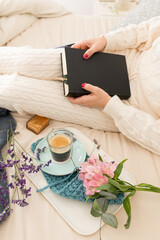 Woman dressed on comfortable loungewear holding a closed book on bed next to her coffee breakfast.