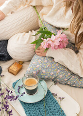 Woman dressed in wool loungewear with a bouquet of flowers in her lap having a cup of coffee.