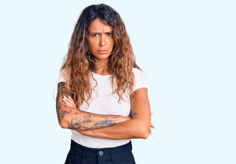 Young hispanic woman with tattoo wearing casual white tshirt skeptic and nervous, disapproving expression on face with crossed arms. negative person.