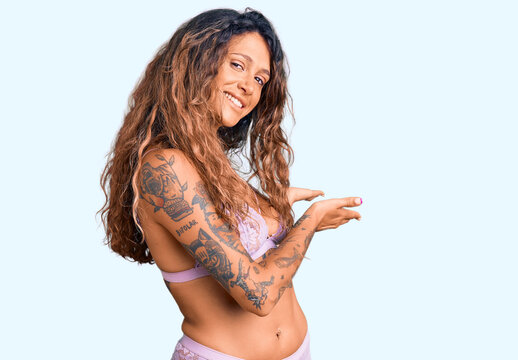 Young hispanic woman with tattoo wearing lingerie inviting to enter smiling natural with open hand