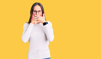 Beautiful brunette young woman wearing casual white sweater and glasses shocked covering mouth with hands for mistake. secret concept.