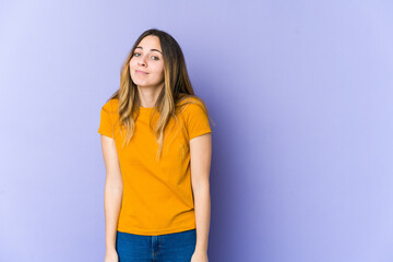Young caucasian woman isolated on purple background shrugs shoulders and open eyes confused.