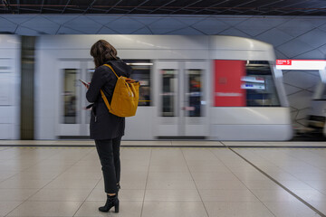 Selective focus at woman with winter jacket and yellow backpack stand, wait and focus on her mobile...