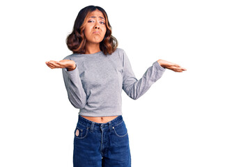 Young beautiful mixed race woman wearing casual clothes clueless and confused expression with arms...