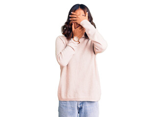 Young beautiful mixed race woman wearing winter turtleneck sweater covering eyes and mouth with hands, surprised and shocked. hiding emotion