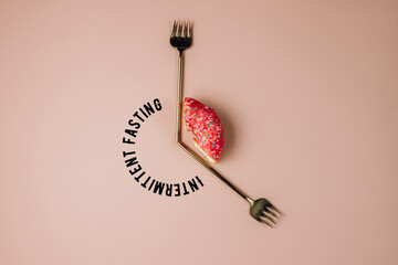 Intermittent fasting concept. One-third donut symbolizing eight hours with cutlery like a clock hands on pink background.