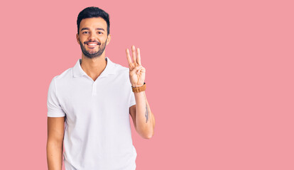 Young handsome hispanic man wearing casual clothes showing and pointing up with fingers number three while smiling confident and happy.