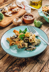 Casserole with pasta, mushrooms, broccoli sauce and cheese on a rustic wooden background.