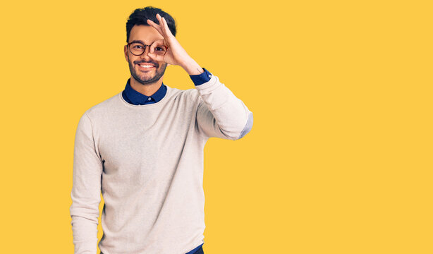 Young handsome hispanic man wearing elegant clothes and glasses doing ok gesture with hand smiling, eye looking through fingers with happy face.