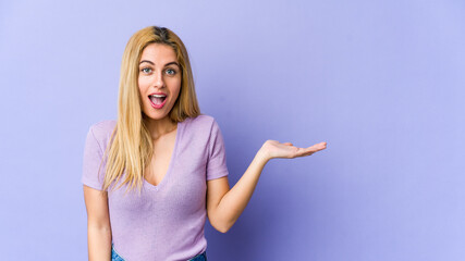 Young blonde caucasian woman impressed holding copy space on palm.