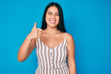 Young beautiful asian girl wearing casual clothes doing happy thumbs up gesture with hand. approving expression looking at the camera showing success.