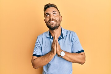 Handsome man with beard wearing casual clothes begging and praying with hands together with hope...