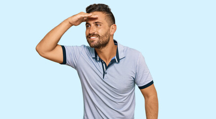 Fototapeta premium Handsome man with beard wearing casual clothes very happy and smiling looking far away with hand over head. searching concept.
