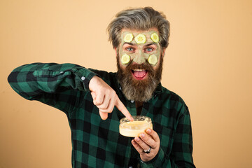 Funny man in a face mask in a beauty salon. Beautician applying scrub onto young mans face in spa. Bearded man having cosmetic mask.
