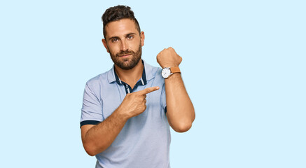 Handsome man with beard wearing casual clothes in hurry pointing to watch time, impatience, looking...