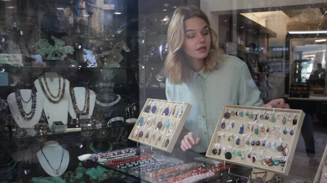Portrait of young woman looking at showcase with natural stone jewelry 