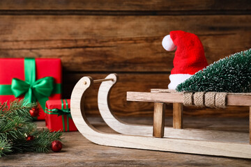 Obraz premium Sleigh with decorative Christmas tree and Santa hat on wooden table