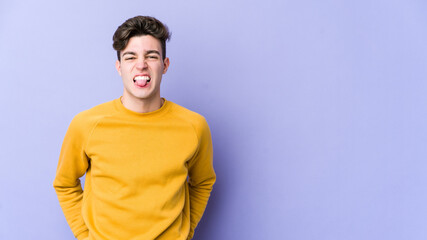 Young caucasian man isolated on purple background funny and friendly sticking out tongue.