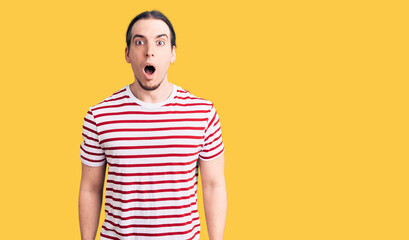 Young adult man with long hair wearing casual striped tshirt scared and amazed with open mouth for surprise, disbelief face