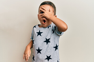 Adorable latin toddler wearing casual clothes peeking in shock covering face and eyes with hand,...