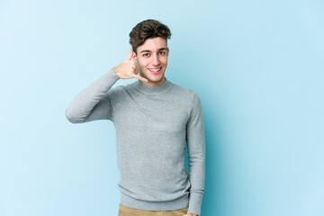 Young caucasian man isolated on blue background showing a mobile phone call gesture with fingers.