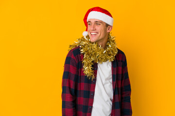 Young caucasian man with christmas hat holding a present isolated on yellow background