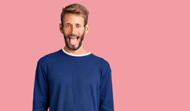 Handsome blond man with beard wearing casual sweater sticking tongue out happy with funny expression. emotion concept.