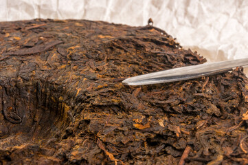 Chinese pressed PU-erh tea on wrapping paper and tea knife, close-up, macro