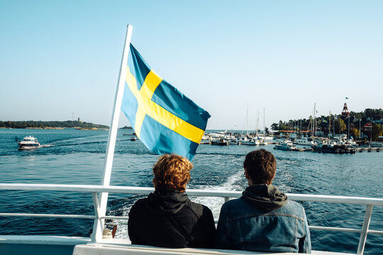View of two people looking out at the Island of Sandhamn with Swedish flag in the background. Stockholm Archipelago, Sweden