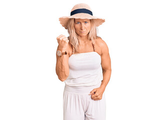 Fototapeta premium Middle age fit blonde woman wearing summer hat angry and mad raising fist frustrated and furious while shouting with anger. rage and aggressive concept.