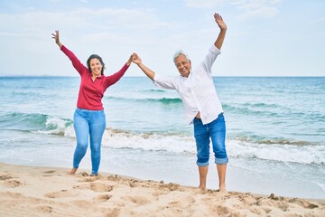 Middle age hispanic couple breathing with arms raised at the beach.