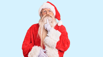 Old senior man with grey hair and long beard wearing traditional santa claus costume thinking concentrated about doubt with finger on chin and looking up wondering