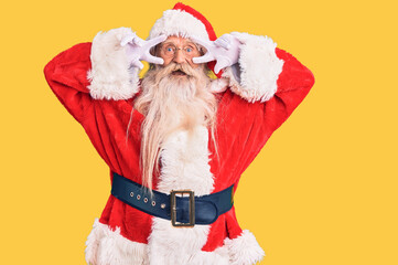 Old senior man with grey hair and long beard wearing traditional santa claus costume doing peace symbol with fingers over face, smiling cheerful showing victory