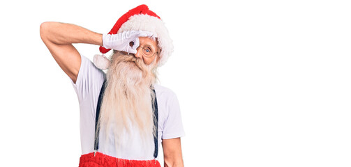 Old senior man with grey hair and long beard wearing santa claus costume with suspenders smiling happy doing ok sign with hand on eye looking through fingers
