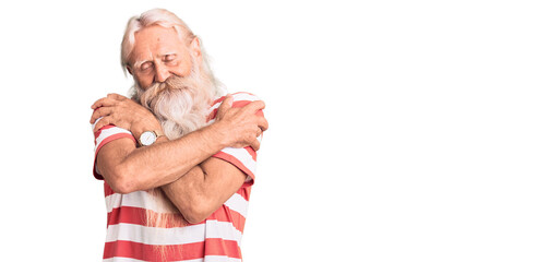 Old senior man with grey hair and long beard wearing striped tshirt hugging oneself happy and positive, smiling confident. self love and self care