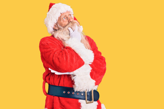 Old senior man with grey hair and long beard wearing traditional santa claus costume with hand on chin thinking about question, pensive expression. smiling with thoughtful face. doubt concept.