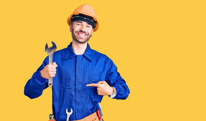 Young hispanic man wearing electrician uniform holding wrench pointing finger to one self smiling happy and proud